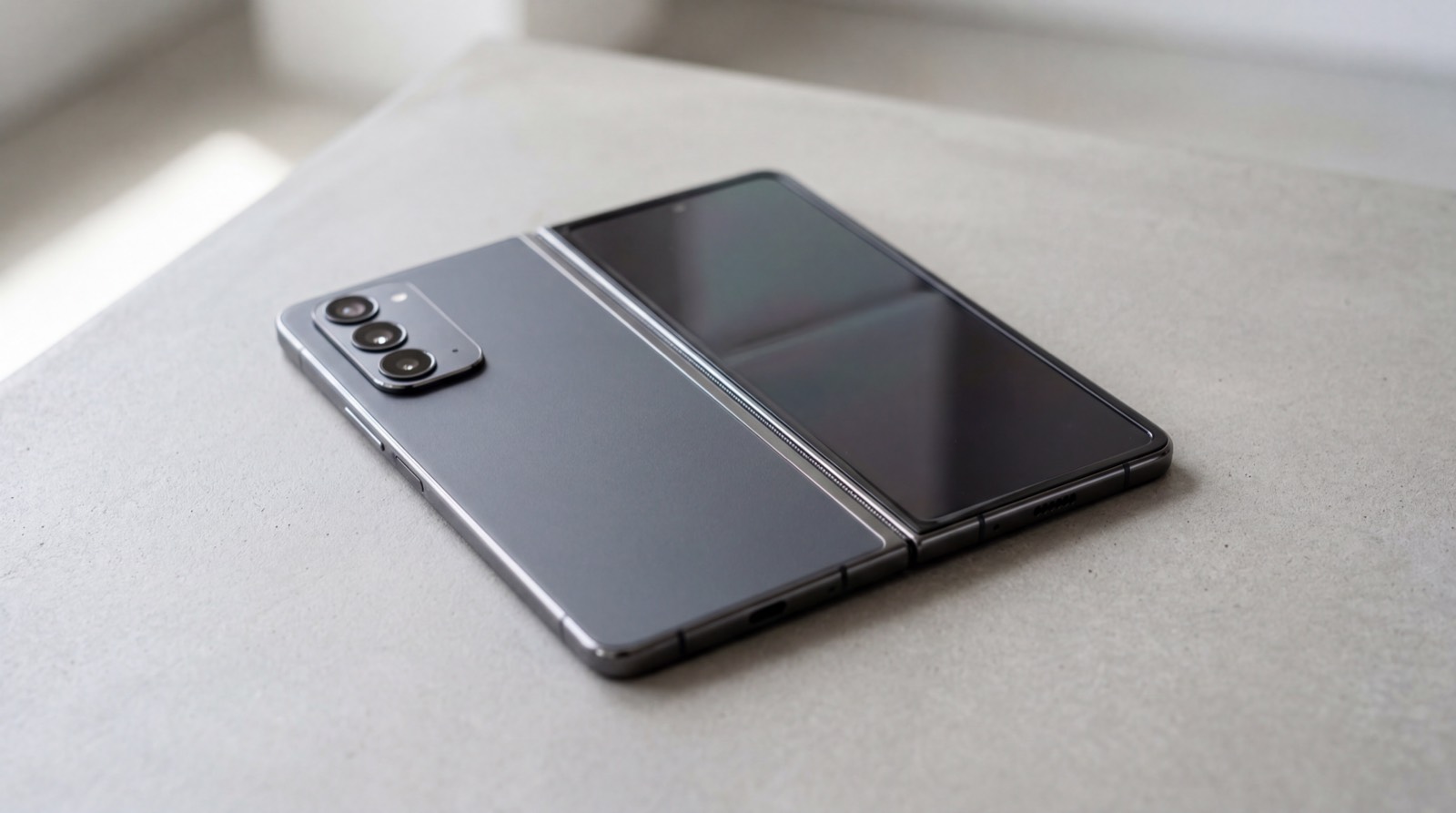 A premium foldable smartphone shown partially unfolded on a clean studio surface.